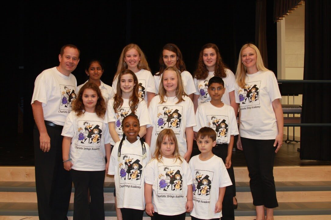 Charlotte Strings Academy teachers and students in matching academy T-shirts on stage
